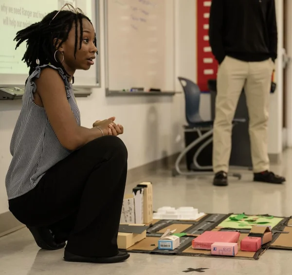 NSBE SEEK Mentor kneeling next to a town prototype for the AI and Robotics Project